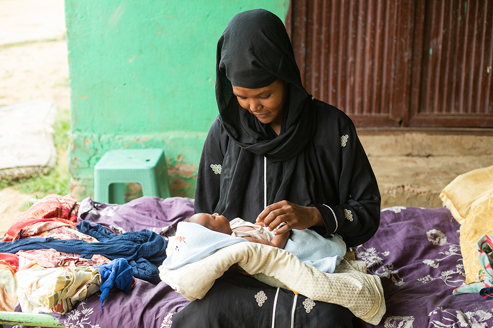 A woman sits with a newborn baby on her lap.