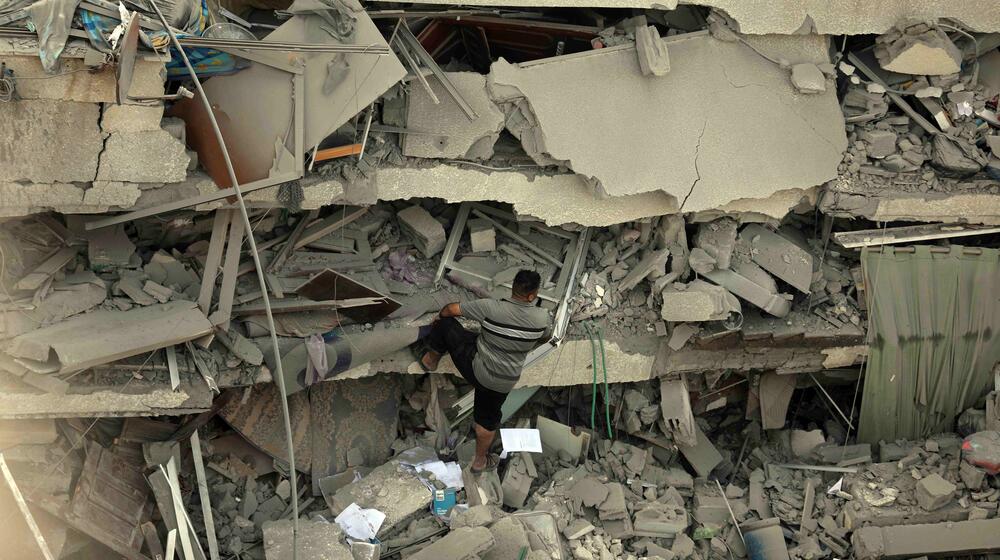 A man climbs on rubble over the destroyed foundation of a heavily bombed building.
