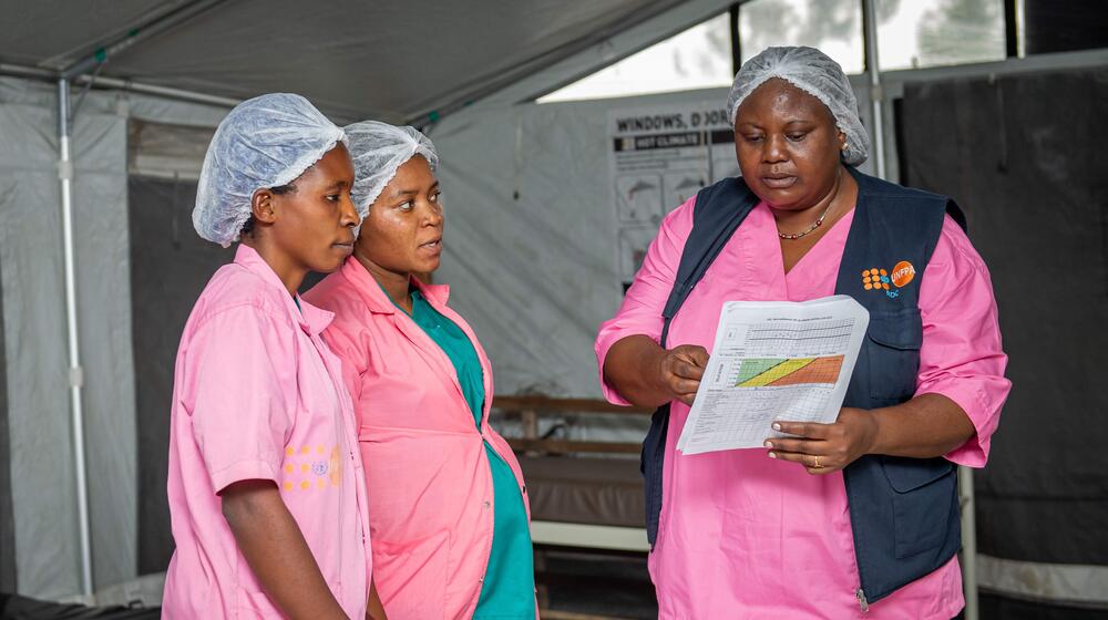 Three midwives discuss medical records in a medical facility.