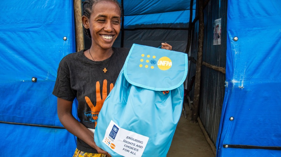 A woman smiles whilst holding a dignity kit.