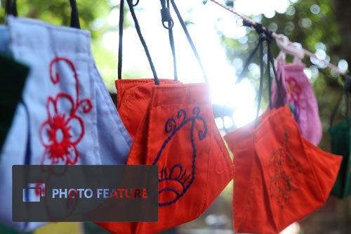 Embroidered cloth face masks hang on a laundry line.