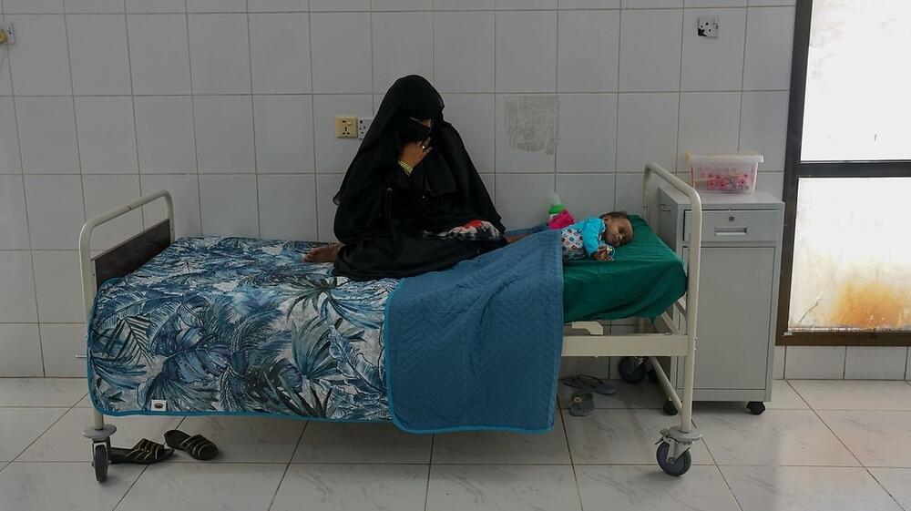 A mother sits with her child at a medical facility.