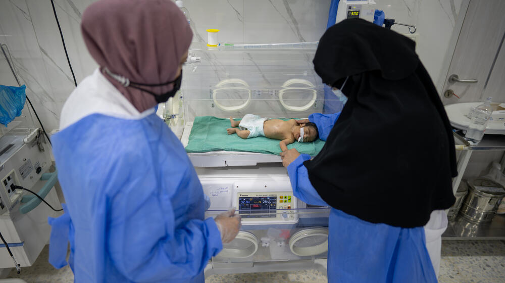 Two healthcare workers monitor a newborn baby.