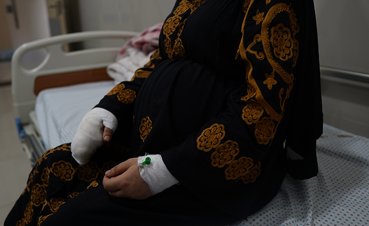 A woman sits on a hospital bed, both of her hands are bandaged.