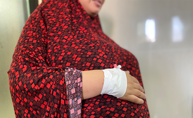 A pregnant woman rests her bandaged hands on her body, caressing her stomach.