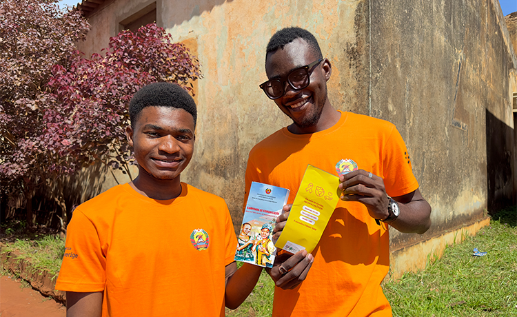 Two young men in orange tee-shirts hold up brochures.