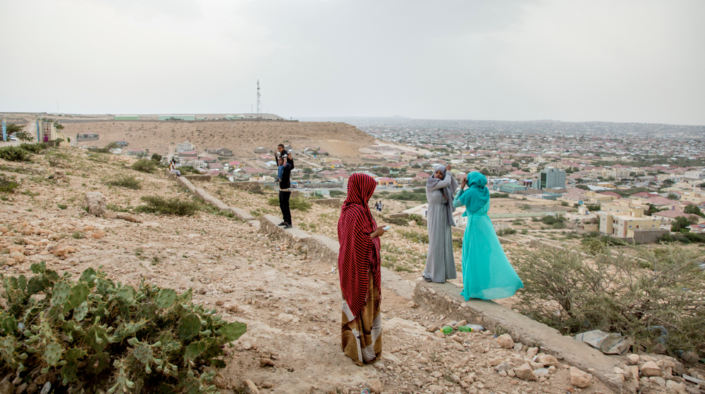 Three Somali women stand on a hill and adjust their hijabs whilst overlooking a town