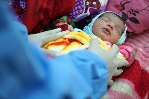 A close up photo shows a newborn baby wrapped in blankets.