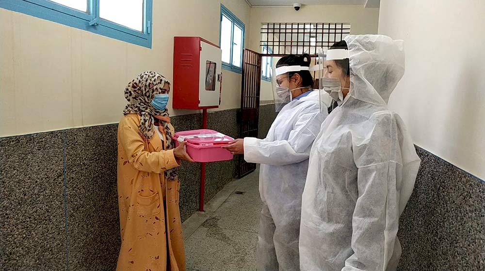Health personnel in personal protective equipment accept a SALAMA kit, a pink plastic tub containing COVID-19 prevention supplies.