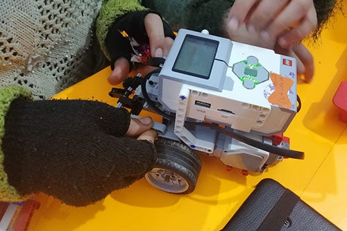 Girls' hands are seen working on a robot together at a women's and girls' safe space. 