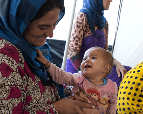 A refugee woman plays with a baby girl in a women's centre.
