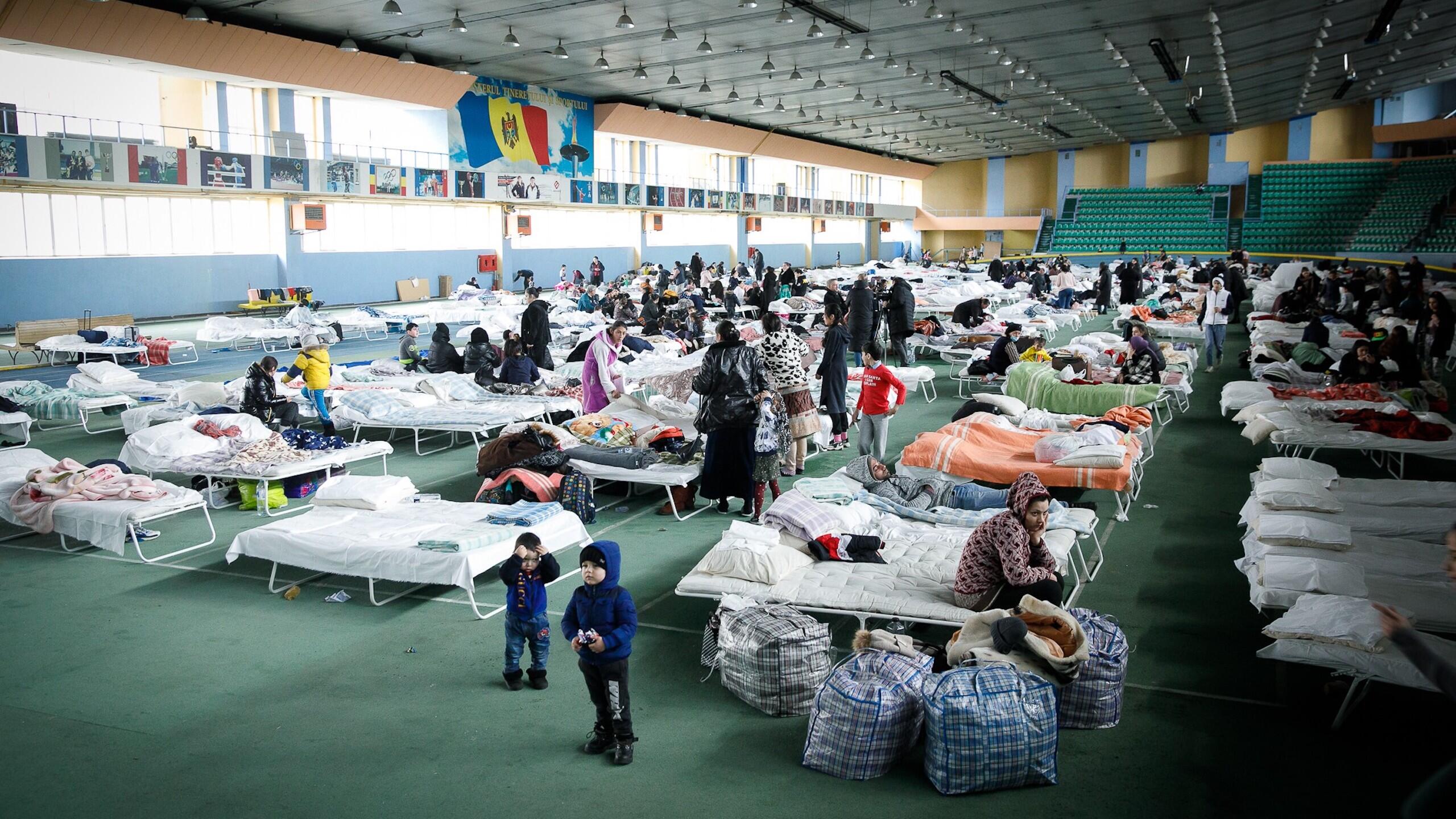 Women and children inside a gymnasium with makeshift beds. 