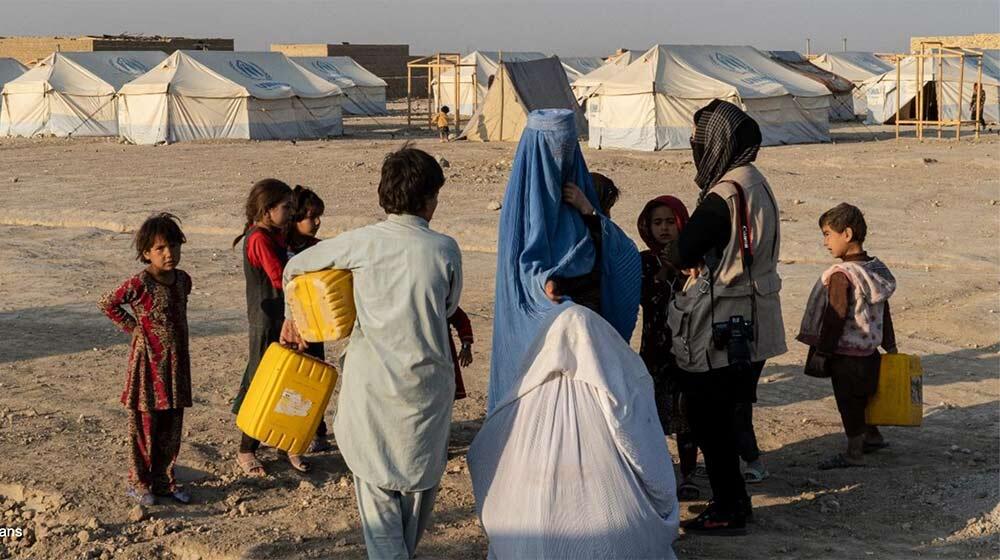 Femme et enfants debout devant des tentes du HCR transportant de l'eau Photo : OCHA/Charlotte Cans
