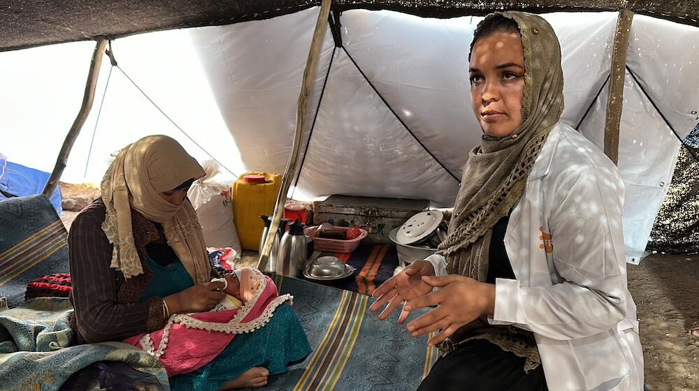 A midwife visits a new mother inside a tent.
