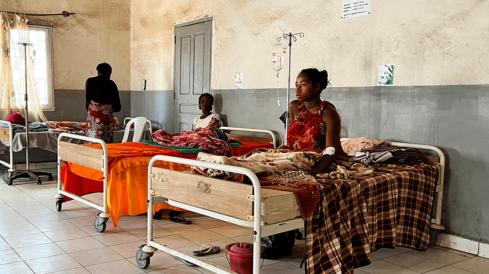 Three women sit on beds in a maternity ward, a fourth stand beside one bed.  