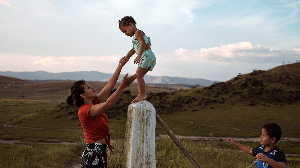 A woman playing with her children surrounded by the rolling green hills of Paracaima, Brazil