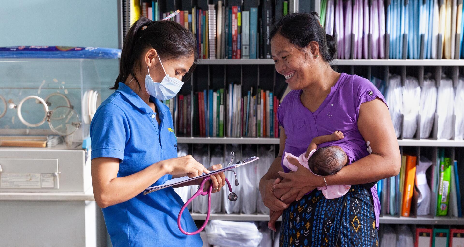A woman breastfeeds and talks to a medical worker.