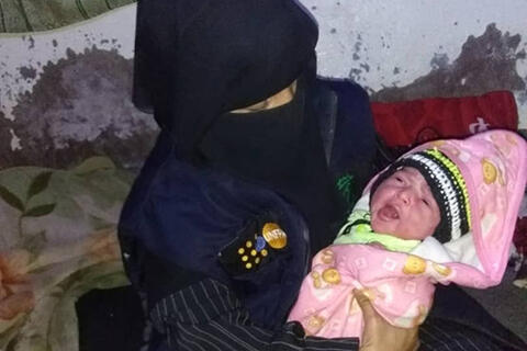 Midwife Al-Shurmani holds a baby swaddled in a pink blanket. The baby is crying.