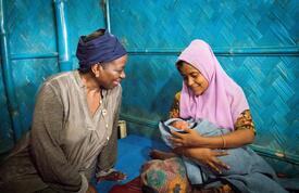 Dr. Natalia Kanem sits to the left of a new mother holding her infant baby in Kutupalong settlement, Bangladesh.